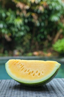 Açık havuz kenarında hasır masada lezzetli bir karpuz dilimi, yakın plan.