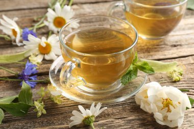 Cam bardaklarda aromatik bitki çayı, ahşap masada nane ve çiçekler, yakın plan.