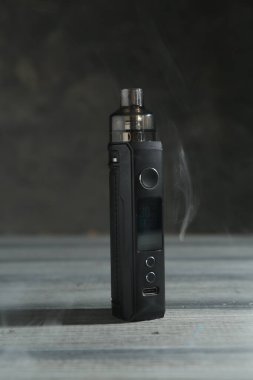 Gri arkaplanlı, yakın plan, ahşap masada dumanlı bir elektronik sigara içme cihazı.