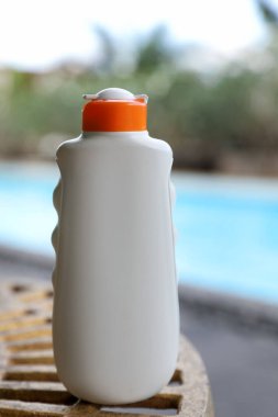 Yüzme havuzunun yakınındaki masada bir şişe güneş koruması ürünü var.