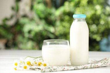Bardakta taze süt, şişe ve beyaz ahşap masada papatya çiçekleri. Süt ürünü