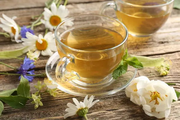 Cam bardaklarda aromatik bitki çayı, ahşap masada nane ve çiçekler, yakın plan.