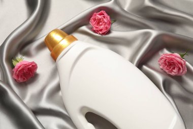 Bir şişe yumuşatıcı ve gri kumaş üzerinde çiçekler, düz yatıyordu.