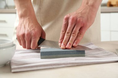 Kapalı alanda bej masa bileyicisiyle bıçak bileyen bir adam.