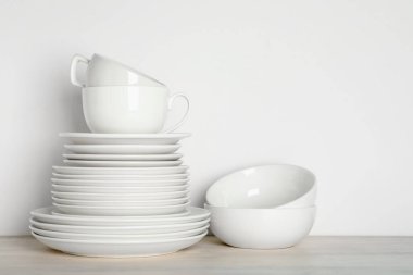 Beyaz duvarın yanındaki açık ahşap masada farklı temiz bulaşık takımı.