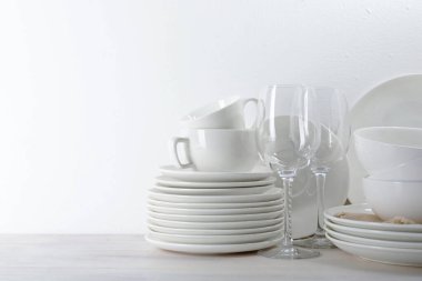 Beyaz duvarın yanındaki açık ahşap masada farklı temiz bulaşık takımı, metin için yer