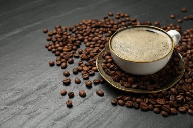 Kahve fincanda, kahve çekirdekleri de siyah masada, yakın plan. Metin için boşluk