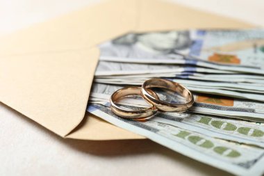 İki altın alyans, bir dolarlık banknotlar ve beyaz masanın üzerindeki zarf, yakın plan.