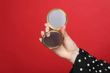 Kırmızı arka planda açık cep aynası tutan kadın, yakın plan.