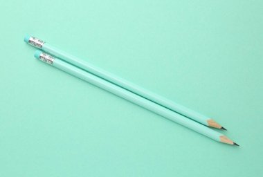 Turkuaz arka planda silgisi olan iki grafit kalem, üst görünüm.