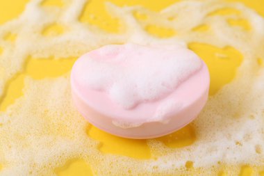 Sarı arka planda köpük olan sabun çubuğu, yakın plan.