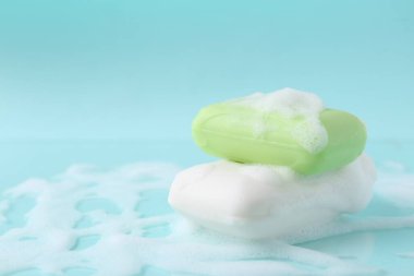 Soap bars with foam on light blue background, closeup. Space for text