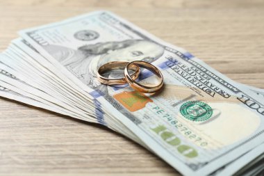 Altın alyanslar ve dolar banknotları ahşap masada, yakın plan.