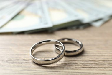 Gümüş alyanslar ve dolar banknotları ahşap masada, yakın plan.