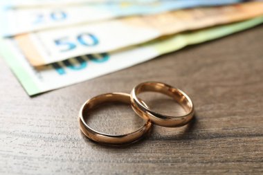 Altın alyanslar ve euro banknotları ahşap masada, yakın plan.