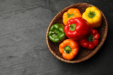 Hasır sepetin içinde taze renkli dolmalık biberler, siyah desenli masa, üst manzara. Metin için boşluk