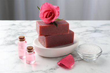 Sabun barları, kozmetik ürünleri ve beyaz mermer masada güzel bir gül.