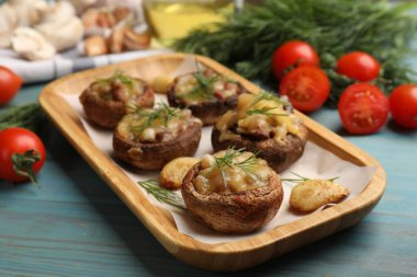 Eritilmiş peynirli, sarımsaklı ve dereotlu leziz mantarlar açık mavi ahşap masada, yakın plan.