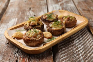 Eritilmiş peynirli, sarımsaklı ve dereotlu lezzetli mantarlar ahşap masa, yakın plan.