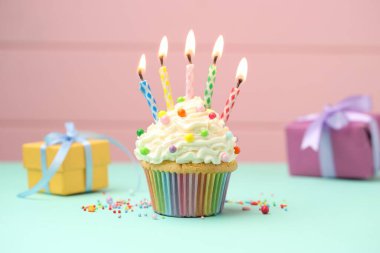 Kekin içinde mum yakmak, serpiştirmek ve pembe arka planda turkuaz masa üzerinde hediye kutuları.