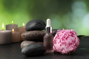 Koyu dokulu masa üzerinde taşlar, damlalar ve çiçekli spa bileşimi bulanık yeşil arkaplan, yakın plan