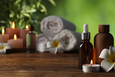 Kozmetik ürünleri, çiçekler ve ahşap masada yanan mumlarla bulanık yeşil arka plan, seçici odak