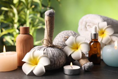 Bitkisel poşetlerle kaplıca kompozisyonu, mum yakan kozmetik ürünleri ve gri desenli masadaki güllük gülistanlık çiçekleri bulanık yeşil arka plan, yakın plan