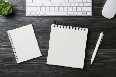 Defterler, kalem, çiçek dekoru, bilgisayar klavyesi ve faresi siyah ahşap masada, düz yatıyordu.