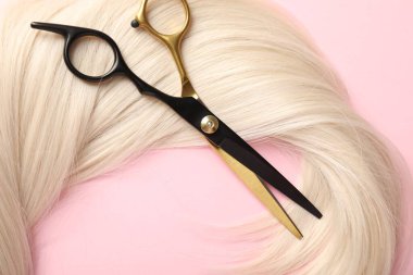 Açık pembe zemin üzerinde saç teli ve makas, üst görünüm