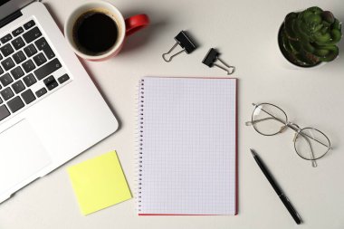 Not defteri, yapışkan not, kalem, çiçek dekoru, bardaklar, kahve ve dizüstü bilgisayar beyaz masada, düz yatıyordu.