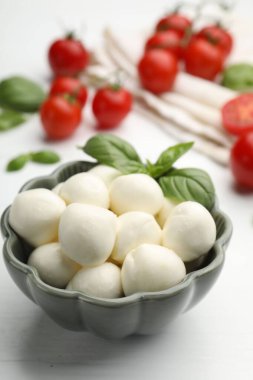 Lezzetli mozzarella peynir topları, domates ve fesleğen beyaz ahşap masada, yakın plan.