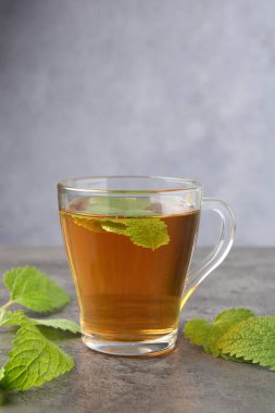 Cam bardakta Aromatik limon merhemi çayı ve gri desenli masada taze yapraklar.
