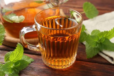 Cam fincanda aromatik limon merhemi çayı, çaydanlık ve ahşap masada taze yapraklar, yakın plan.