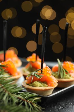 Lezzetli kanepeler ve siyah masa üzerindeki Noel dekoru. Karanlık arka plan, bulanık ışıklar, yakın çekim. Bokeh etkisi