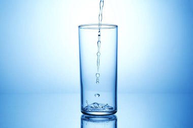 Açık mavi gradyan arkaplana karşı ayna masasında cama su dökmek, yakın plan