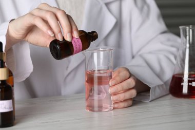 Laboratuvarda beyaz ahşap masada lüks parfüm üreten profesyonel bir parfümcü.