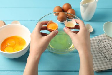 Açık mavi ahşap masada yumurta sarısını beyazdan ayıran kadın, yakın plan.