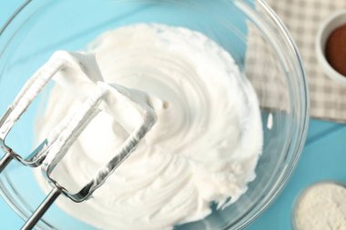 Krem şantili kase, el mikseri ve malzemeler açık mavi ahşap masa, düz yatıyordu.