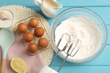 Açık mavi ahşap masa üzerinde çırpılmış krema, yumurta ve diğer ürünlerle el çırpıcı düz yatıyordu.