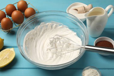 Açık mavi ahşap masa üzerinde çırpılmış krema, yumurta ve diğer ürünlerle çırpın, yakın plan