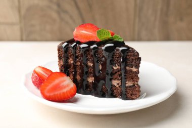 Bir parça çikolatalı kek, beyaz masada çilekli, yakın plan.