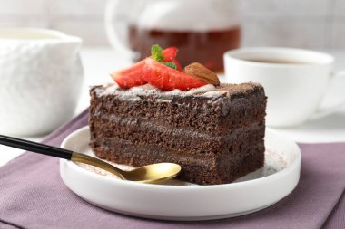 Çilekli, bademli ve masada çay bulunan bir dilim lezzetli çikolatalı pasta.