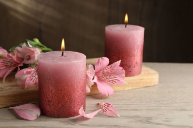 Beyaz ahşap masada yanan mumlar ve zambak çiçekleri, yakın plan.