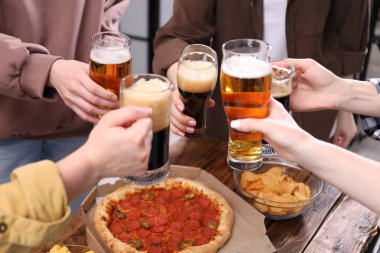 Arkadaşlar ahşap masada bira bardaklarını tokuşturur, yakın plan