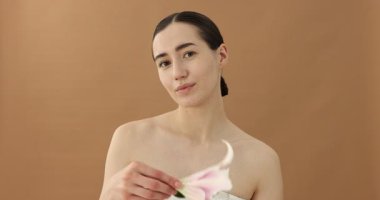 Bej arka planda zambak çiçeğiyle poz veren güzel bir kadın.