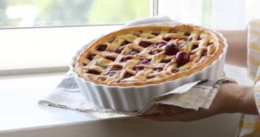 Pencere pervazının yanında nefis vişneli turta tutan kadın, yakın plan.