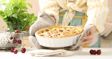 Beyaz ahşap masaya lezzetli vişneli turta koyan kadın, yakın plan.