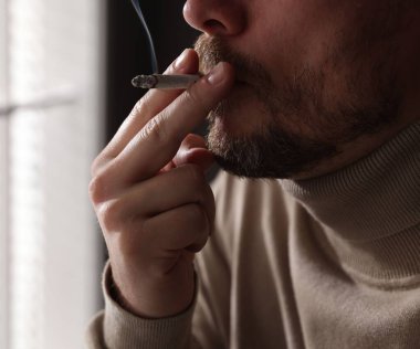 Pencerenin yanında sigara içen adam, yakın plan.