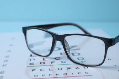 Açık mavi arkaplanda gözlük ve görüş testi grafiği, yakın plan