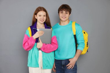 Gri arka planda sırt çantası ve dizüstü bilgisayarı olan gençler.